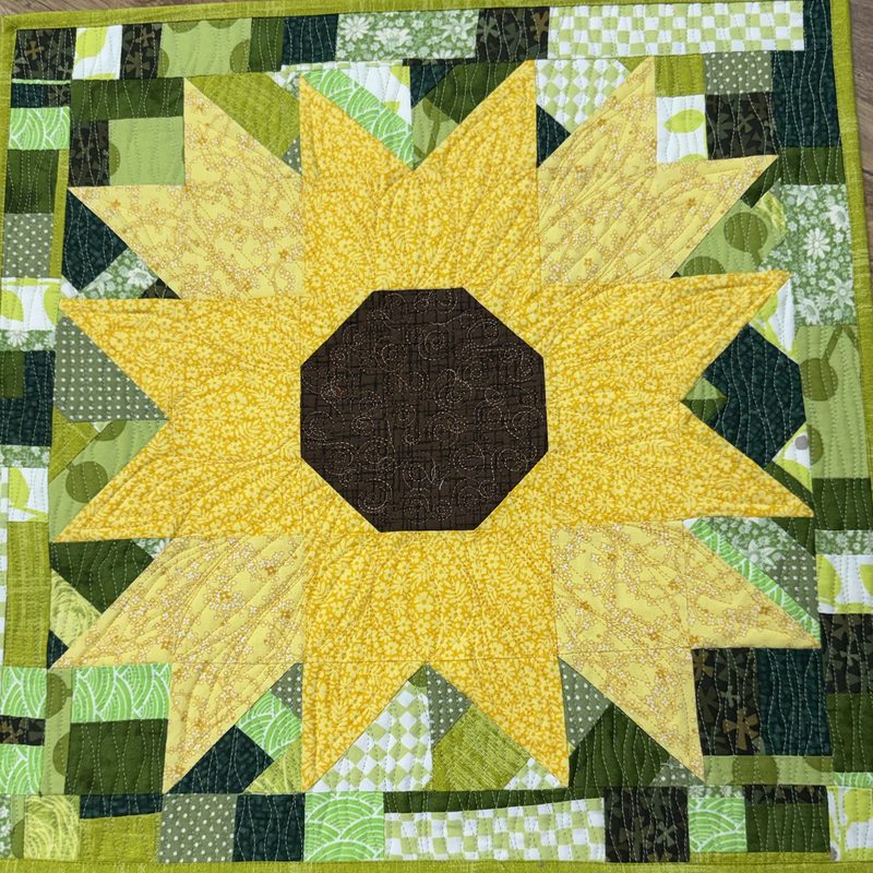 Scrappy improv sunflower quilt with a yellow star flower on a pieced green background